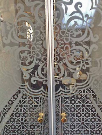 Puerta doble de entrada a baño grabada al ácido con decoración arabesca detalle central